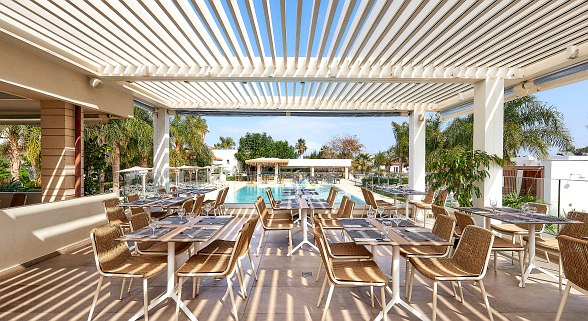 Elegantly laid outdoor table with cutlery, plate, wine glass and water glass, green plants in the background.