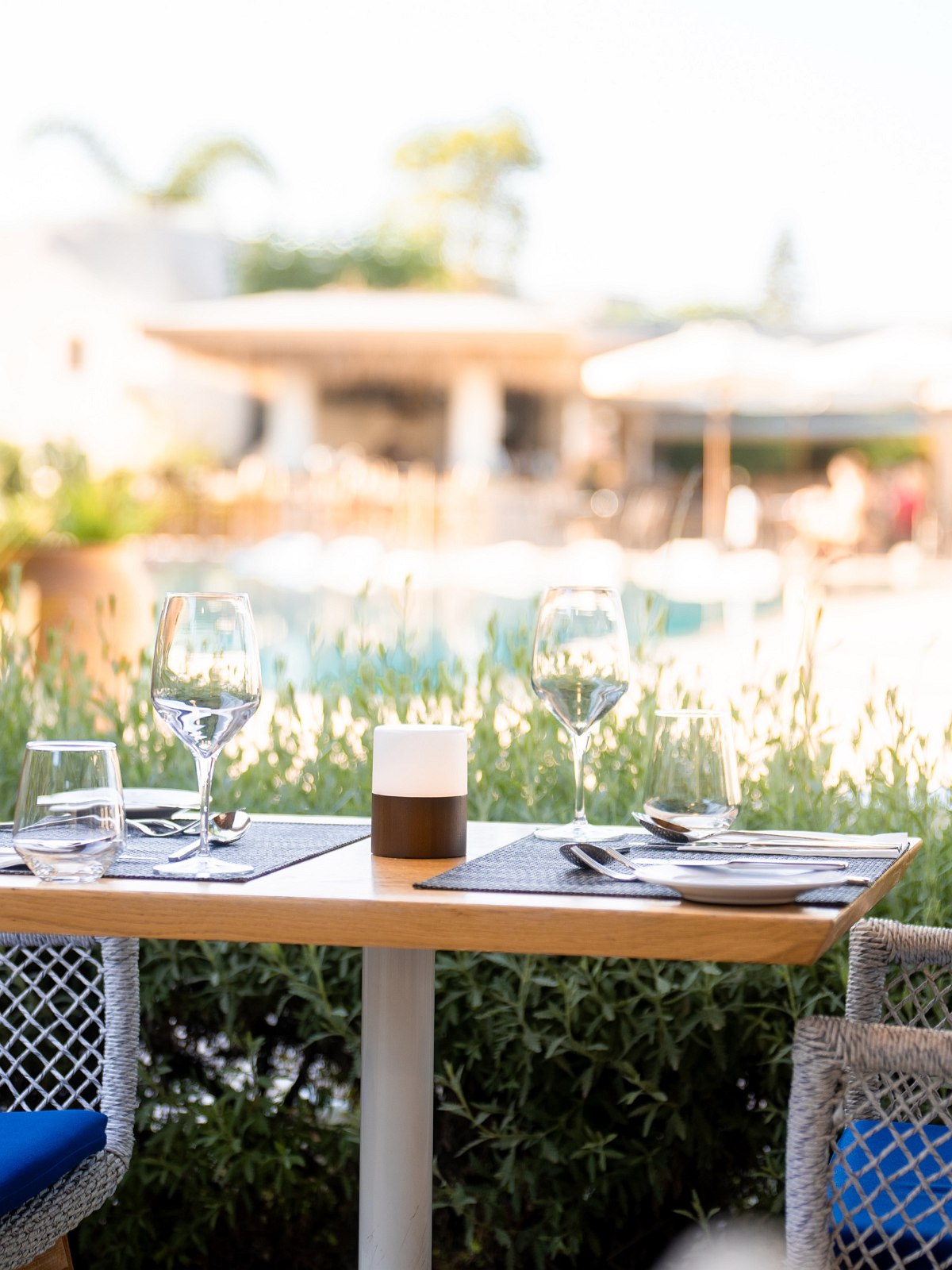 Elegantly laid table in the outdoor area of a restaurant with a view of palm trees, pool and lounge area in the background.