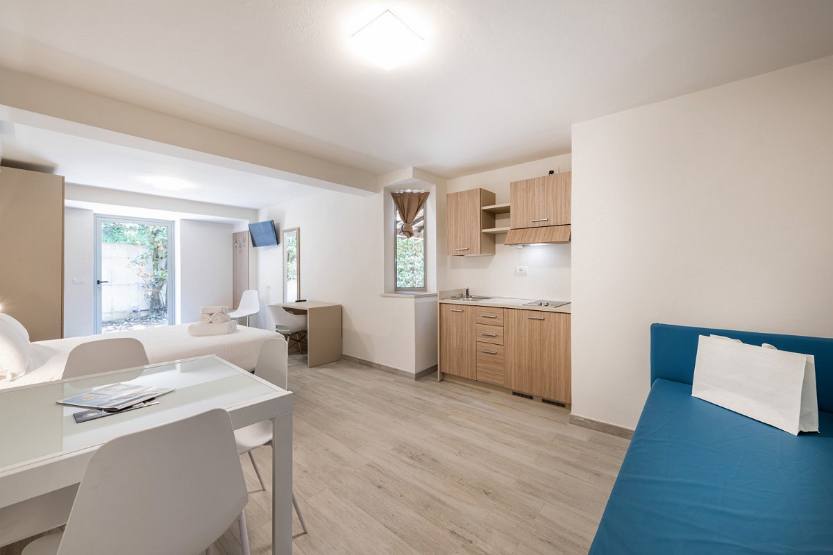 Bright, barrier-free studio apartment with open kitchen, dining table with chairs, sleeping area and a sofa. The furnishings are modern and functional, with ground-level access and generous space