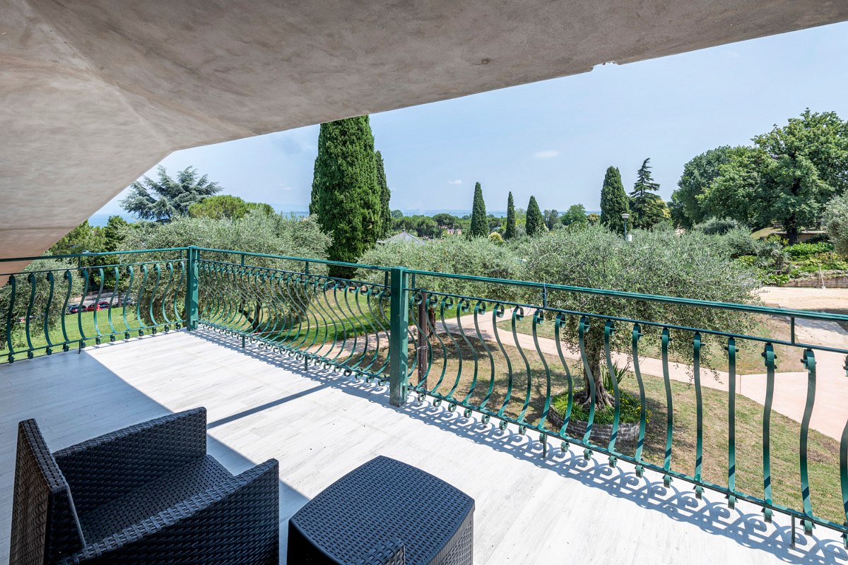 Balcony with hillside-view, seating furniture and view of a well-tended garden with trees and walking paths.