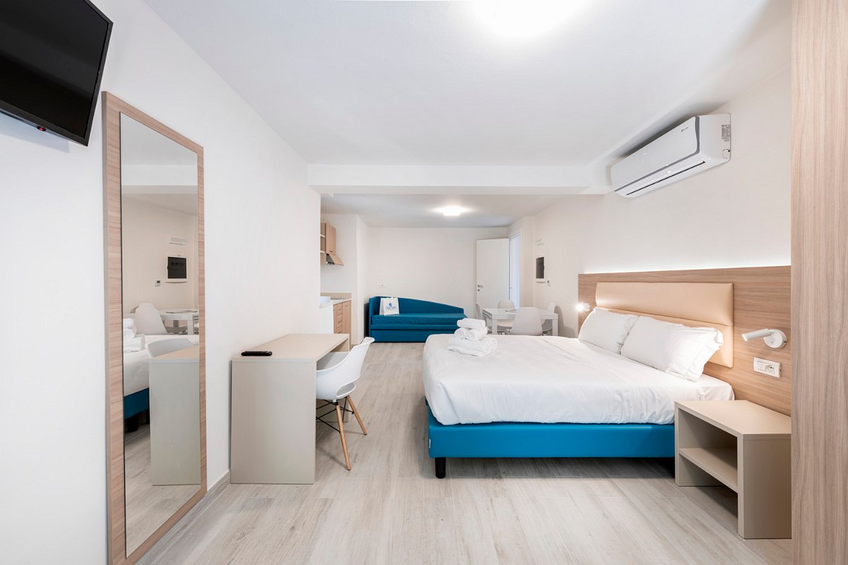 Modern apartment with double bed, turquoise sofa, large mirror, bedside tables, air conditioning, TV and desk.
