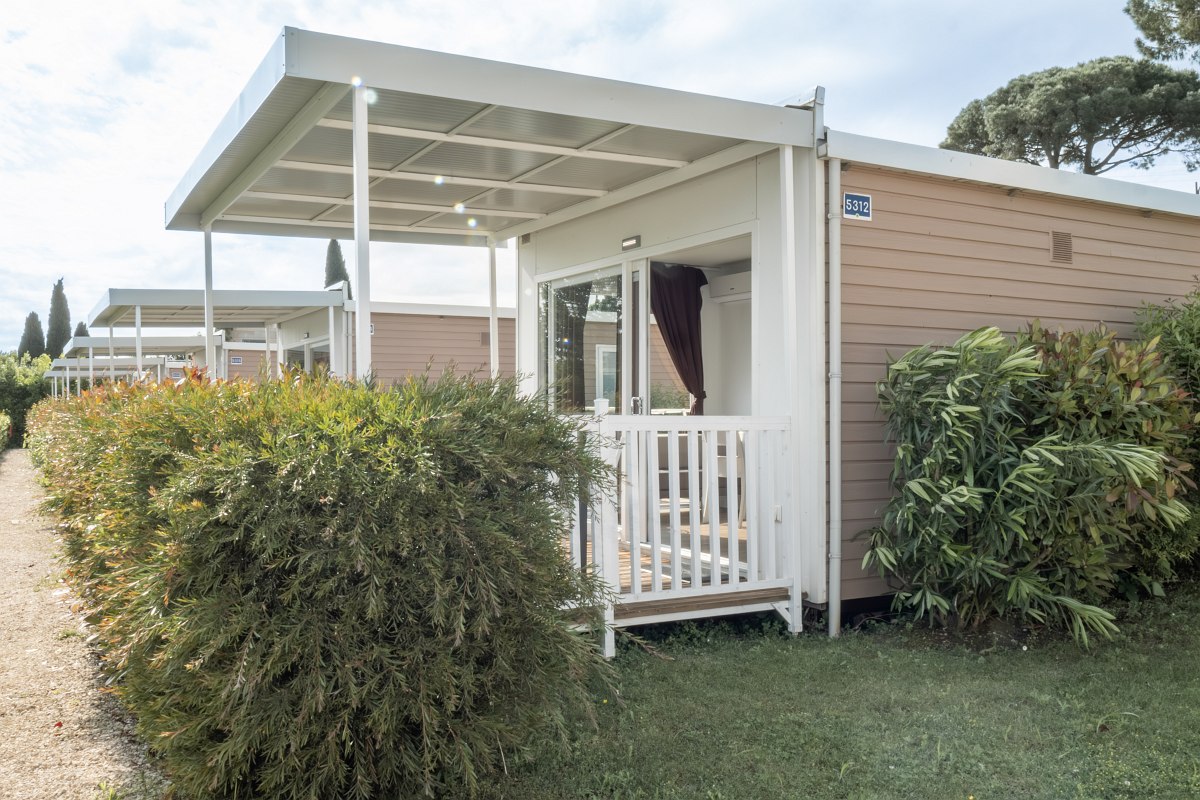 Detached mobile home with covered terrace, surrounded by hedges and lawn - ideal for a vacation close to nature.