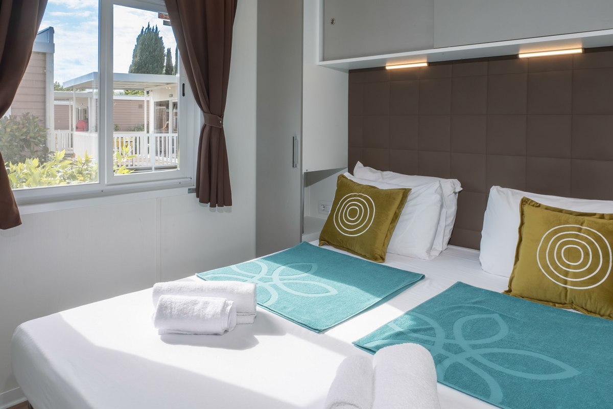 Modern bedroom with double bed, window with curtains, decorative cushions and bedspread in turquoise.