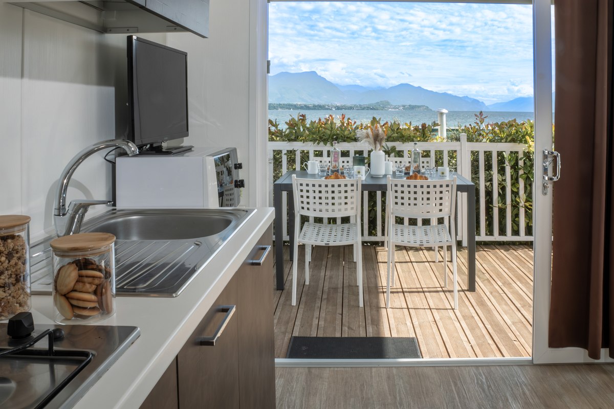 Modern kitchenette overlooking a covered terrace with breakfast table and panoramic views of the mountains and lake.