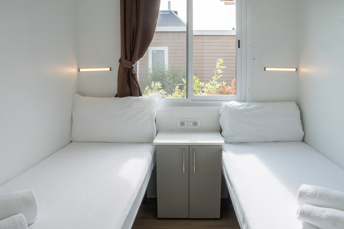 Bright bedroom with two single beds, window with brown curtains and small wardrobe between the beds.