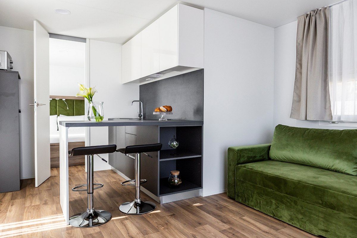 Modern, compact apartment with kitchenette, bar counter with stools, green sofa and wooden floor - bright and cozy.