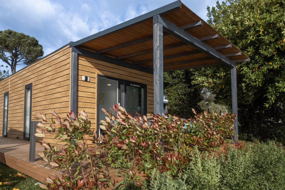 Modern, ground-floor mobile home with wooden cladding, covered terrace and surrounded by well-tended greenery.