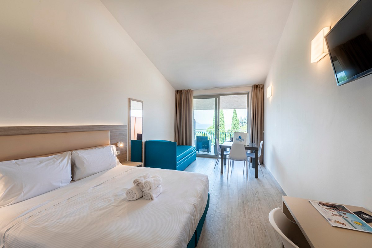 Modern apartment with double bed, turquoise sofa, mirror, TV, table with chairs and access to the furnished balcony terrace overlooking the “Hillside area”.