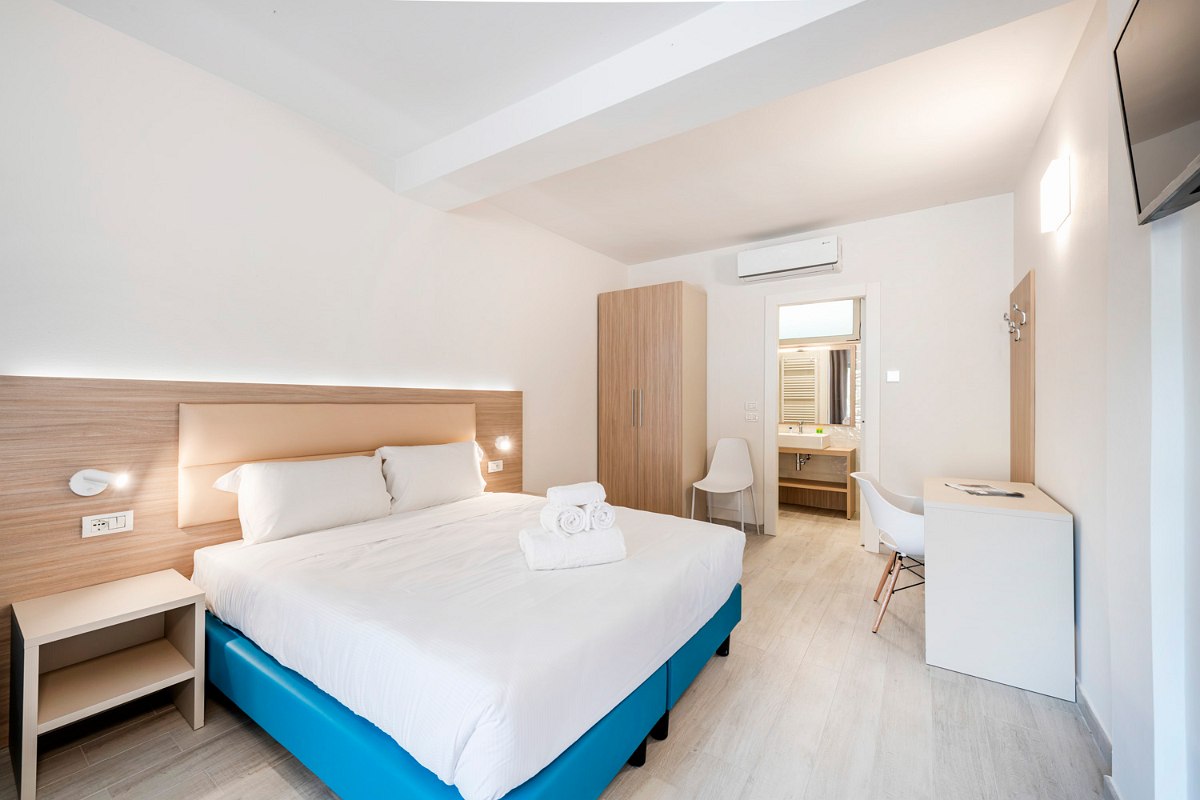 Modern studio with double bed, turquoise sofa, large mirror, bedside tables, air conditioning, TV and desk and lake view.