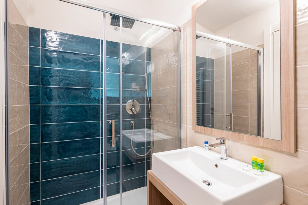 Modern bathroom with walk-in, blue tiled shower, grab rail, washbasin and large mirror.