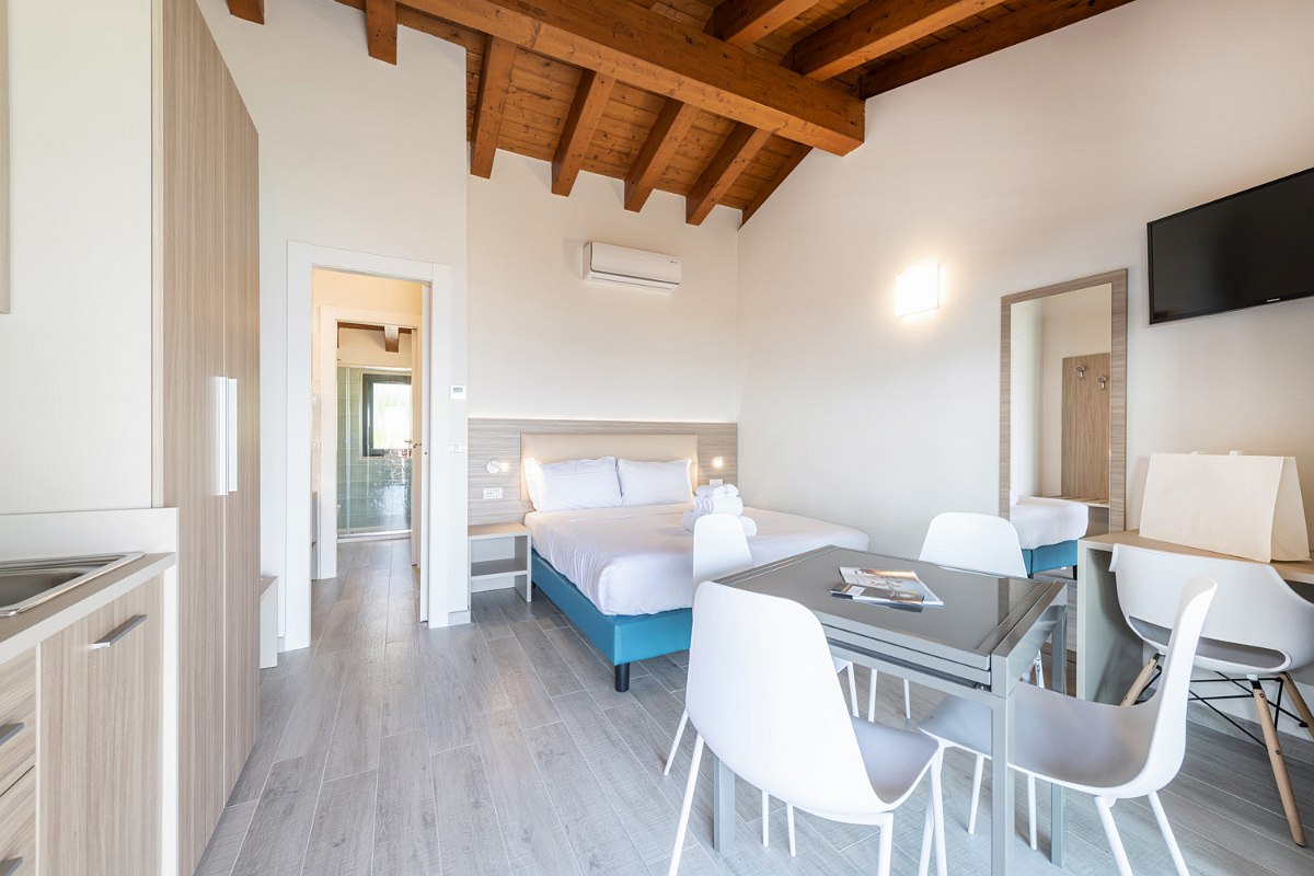 Bright studio with double bed, dining area with tables and chairs, kitchenette and wooden ceiling - modern and comfortably furnished.