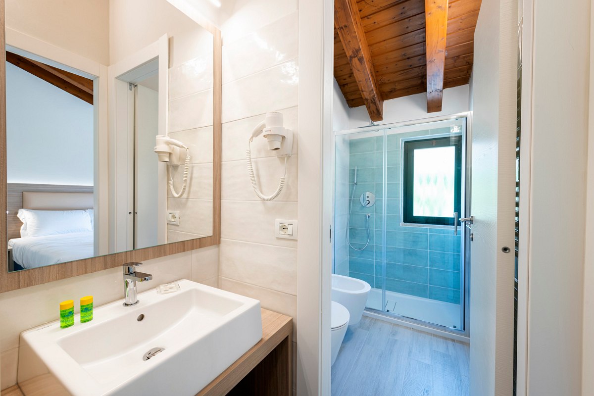 Modern bathroom with 2 seperate rooms, walk-in, blue tiled shower, toilet, hair dryer grab rail, washbasin and large mirror.