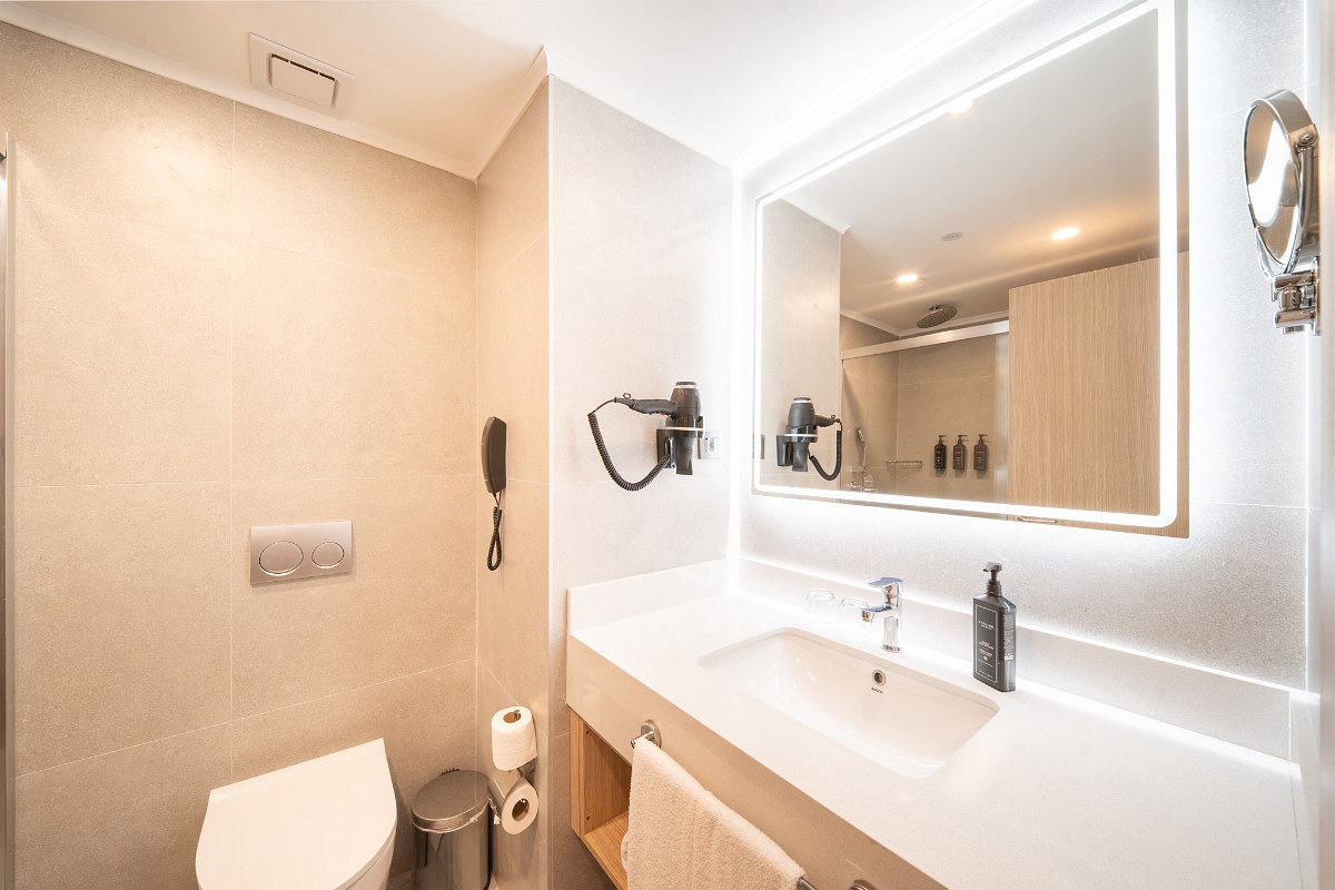 Modern hotel bathroom with glass shower, elegant marble washbasin and high-quality care products.