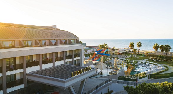 Hotel complex with palm trees, extensive gardens, white towers and views of the deep blue Mediterranean.