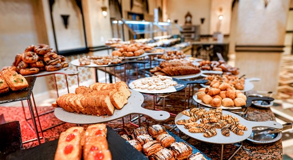 Freshly baked bread, assorted pastries, croissants, sweet treats, muffins, danishes, and cakes arranged beautifully on display for guests to enjoy.