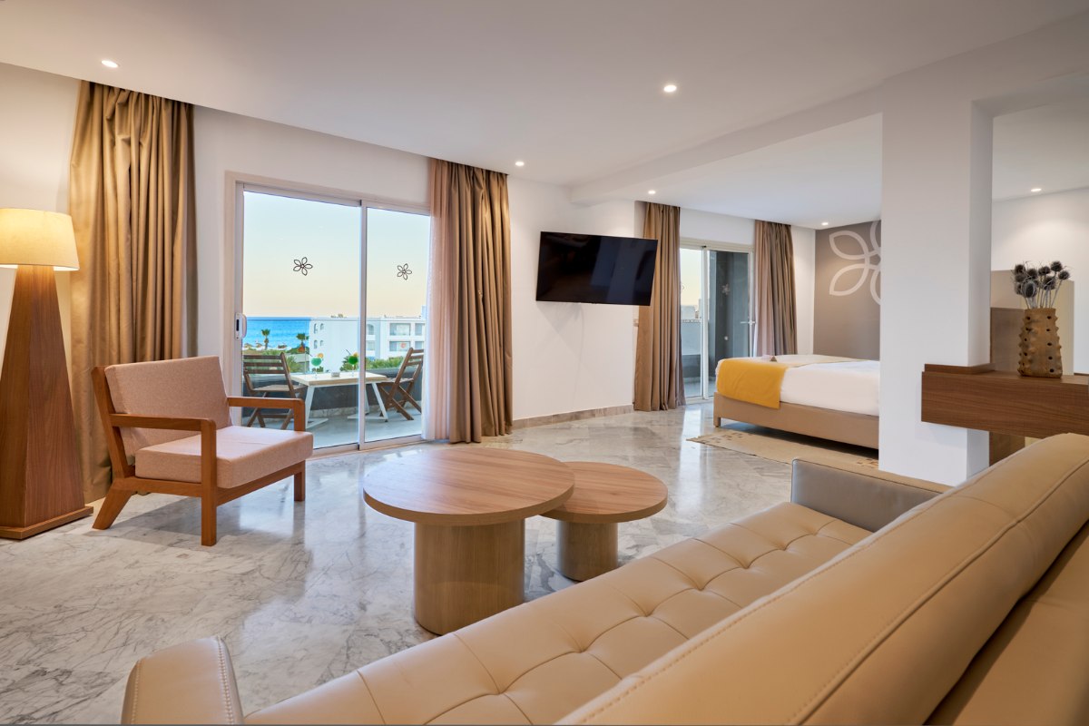 Hotel terrace with comfortable armchairs, wooden floor, private pool and green garden under a sunny sky.