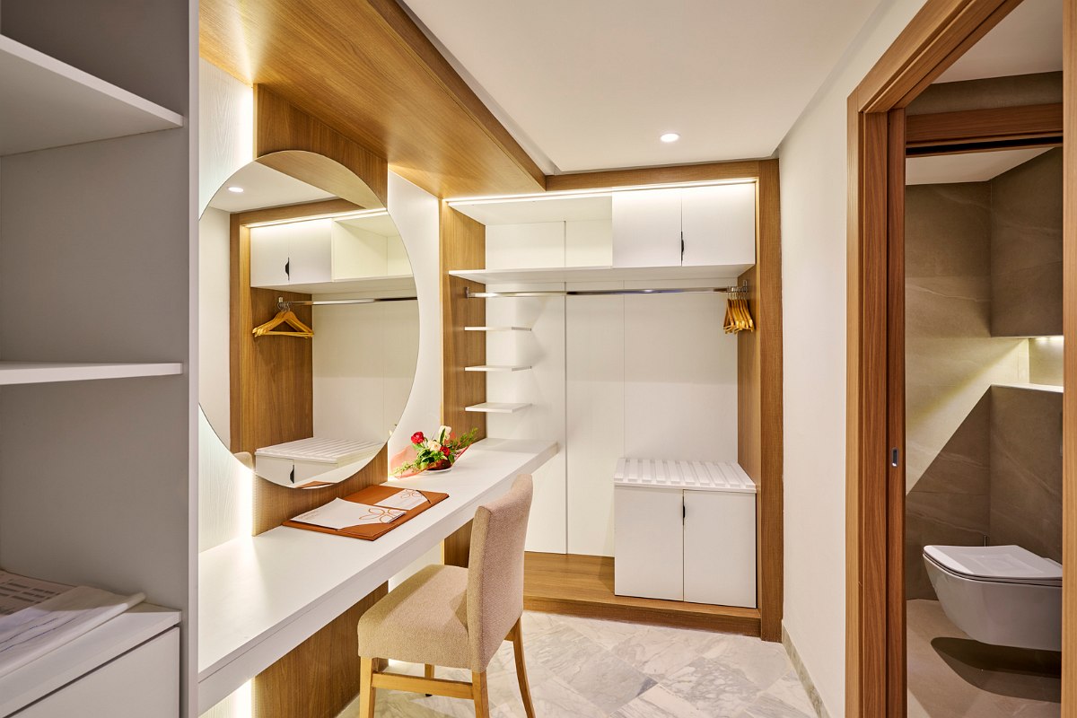 Modern hotel room with large bed, comfortable couch, desk and terrace with pool view.