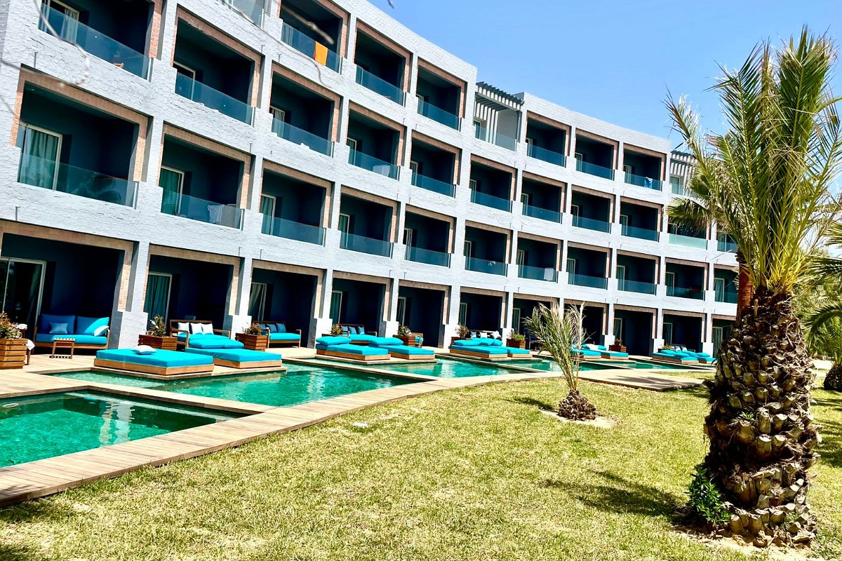 Modern hotel room with large bed, comfortable couch, desk and terrace with pool view.