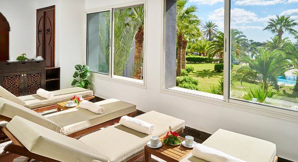 Brightly designed hotel lobby area with high windows, pillars with blue mosaic and palm tree view in the background.