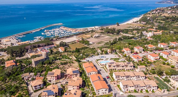 Aerial view of the Sentido Michelizia Tropea Resort with a view of the coastal town of Tropea with its harbour, sandy beach and many houses in a sunny landscape.