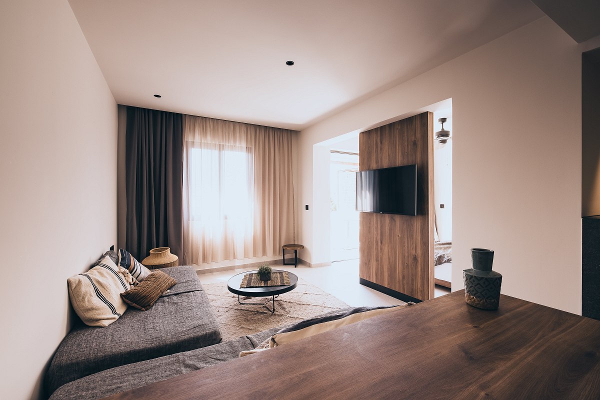 Bright, modern living room in warm tones with grey sofa, round coffee table, wooden details and wall-mounted TV.