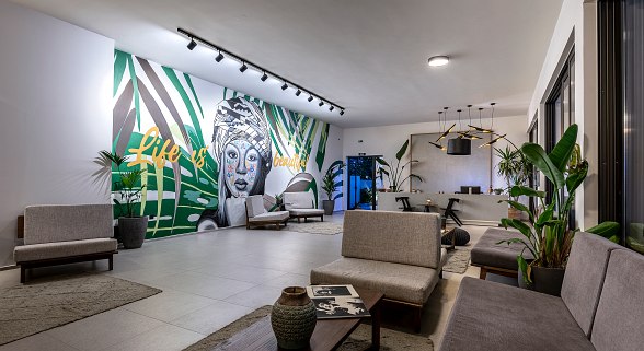 Modern designed hotel lobby with plants, seating areas and a mural of a woman with the text ‘Life is beautiful’.