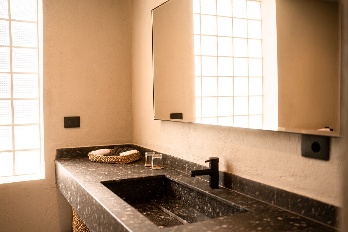 ‘Modern bathroom with dark washbasin, round mirror and walk-in shower with glass door.’
