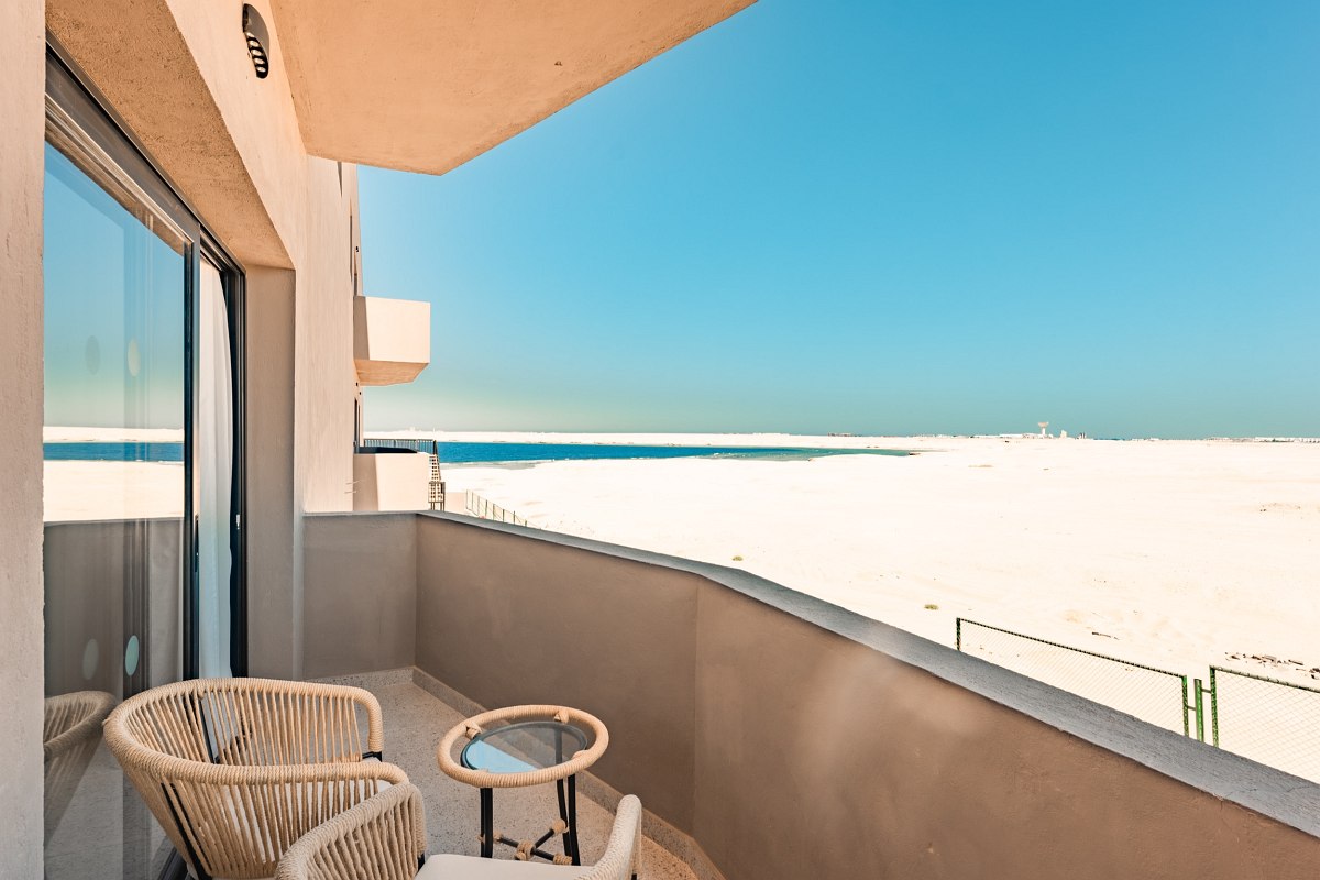 Large terrace with two armchairs, table and sea view under an open sun canopy.