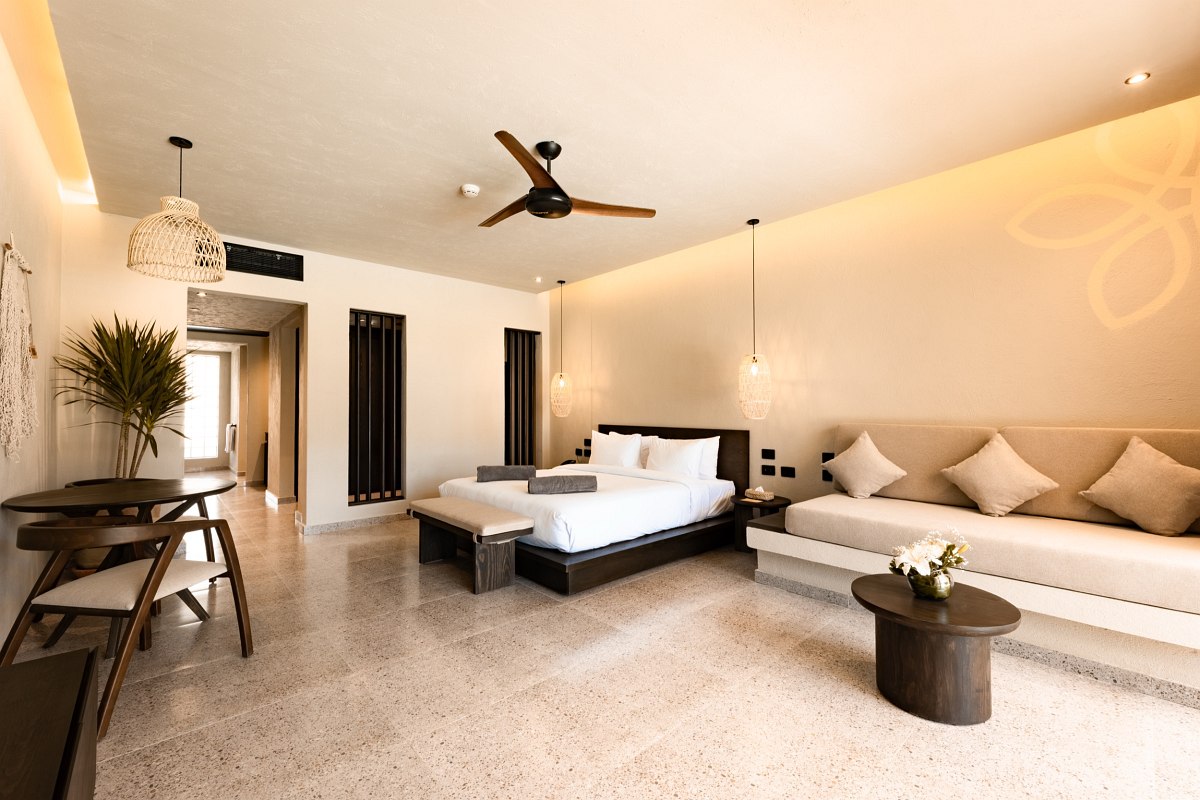 Bright, modern hotel room with large bed, seating area, dining table and balcony with curtains
