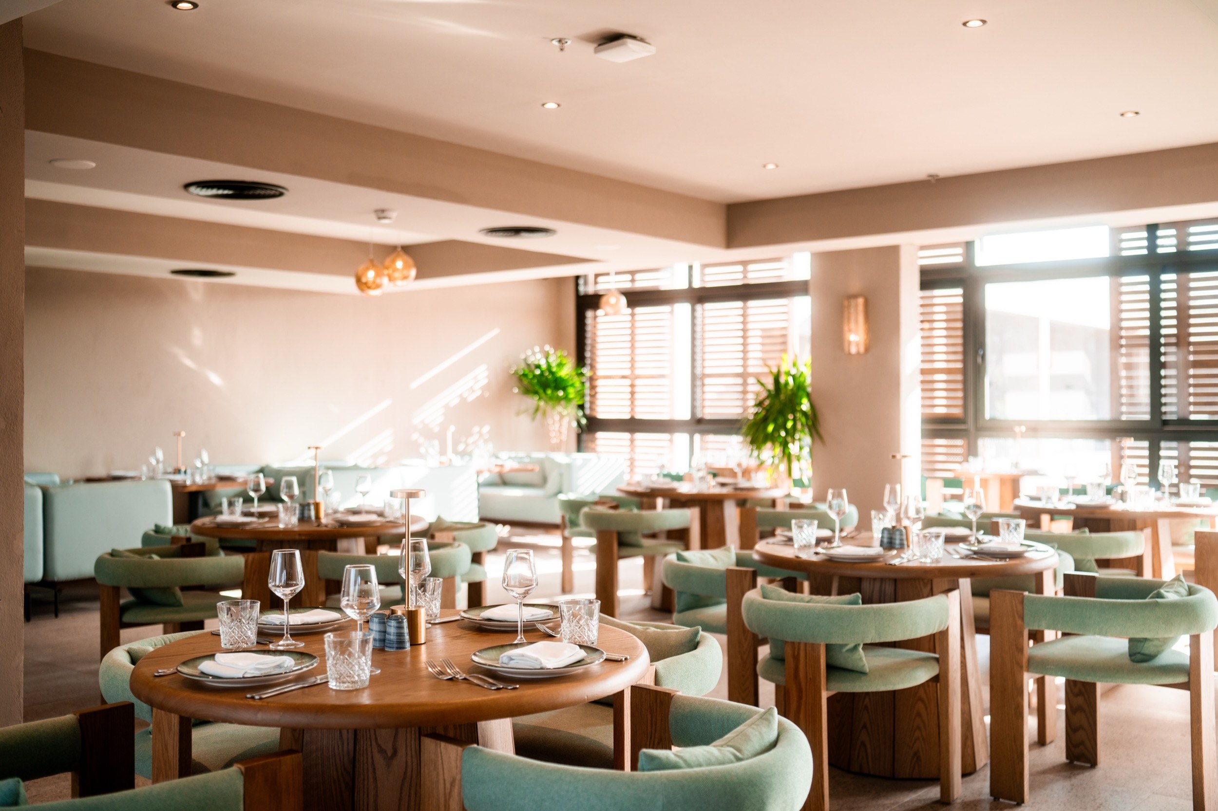 Bright, stylishly furnished restaurant with covered wooden tables, green chairs and large windows.