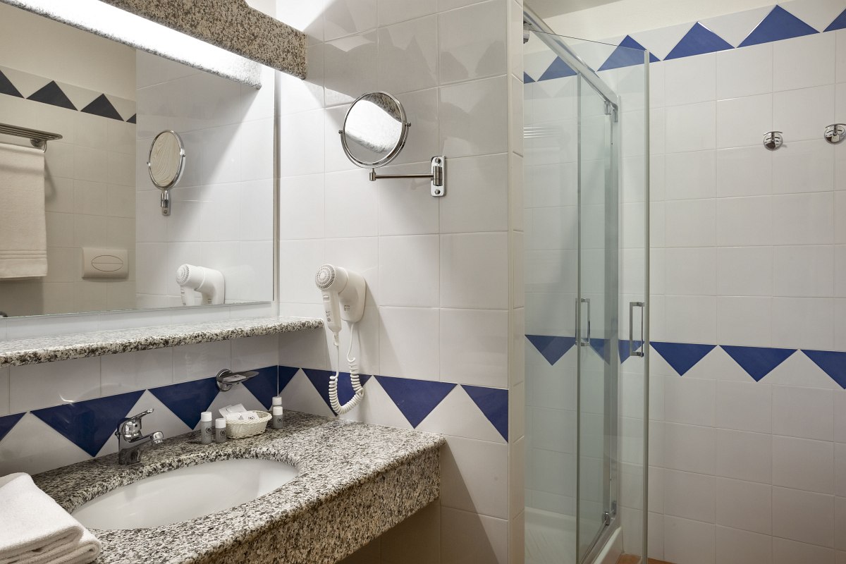 Bright bathroom with large shower, granite washbasin, mirror, vanity mirror, hairdryer and blue and white tiles.