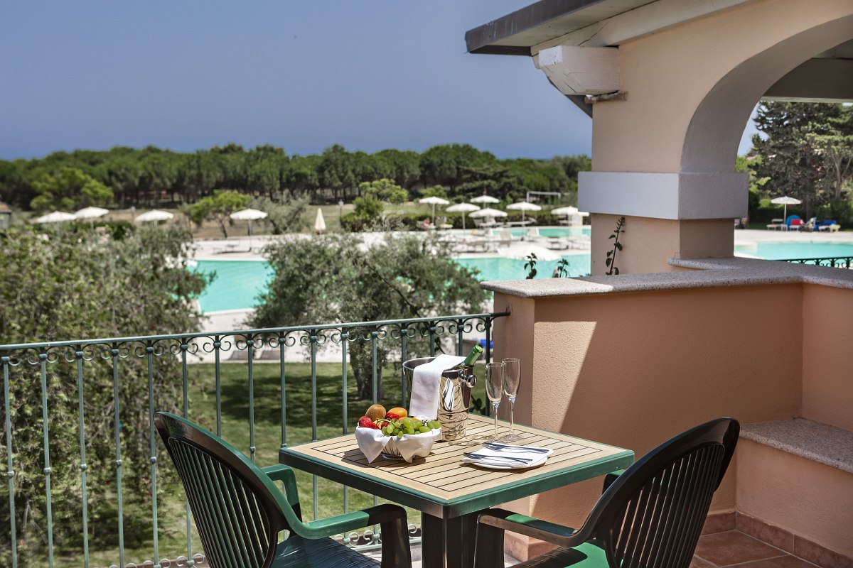 Balcony with seating area and view of the pool landscape, olive trees and pine forest - ideal for breakfast outdoors.