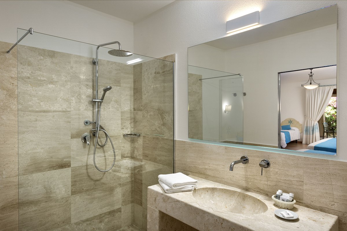 Modern bathroom with large walk-in shower, natural stone washbasin, large mirror and view into the adjoining bedroom.
