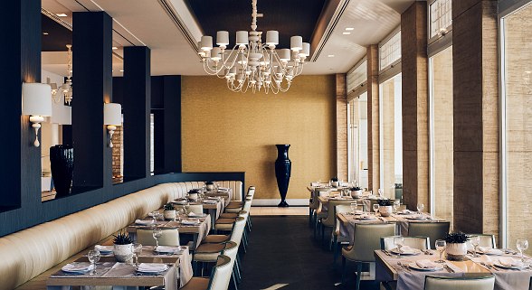 Elegant hotel restaurant with large windows, stylishly laid tables, chandeliers and modern, warm interior design.