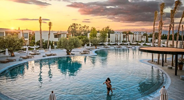 Romantic atmosphere at the large resort pool at sunset, a couple enjoying intimate moments in the water.