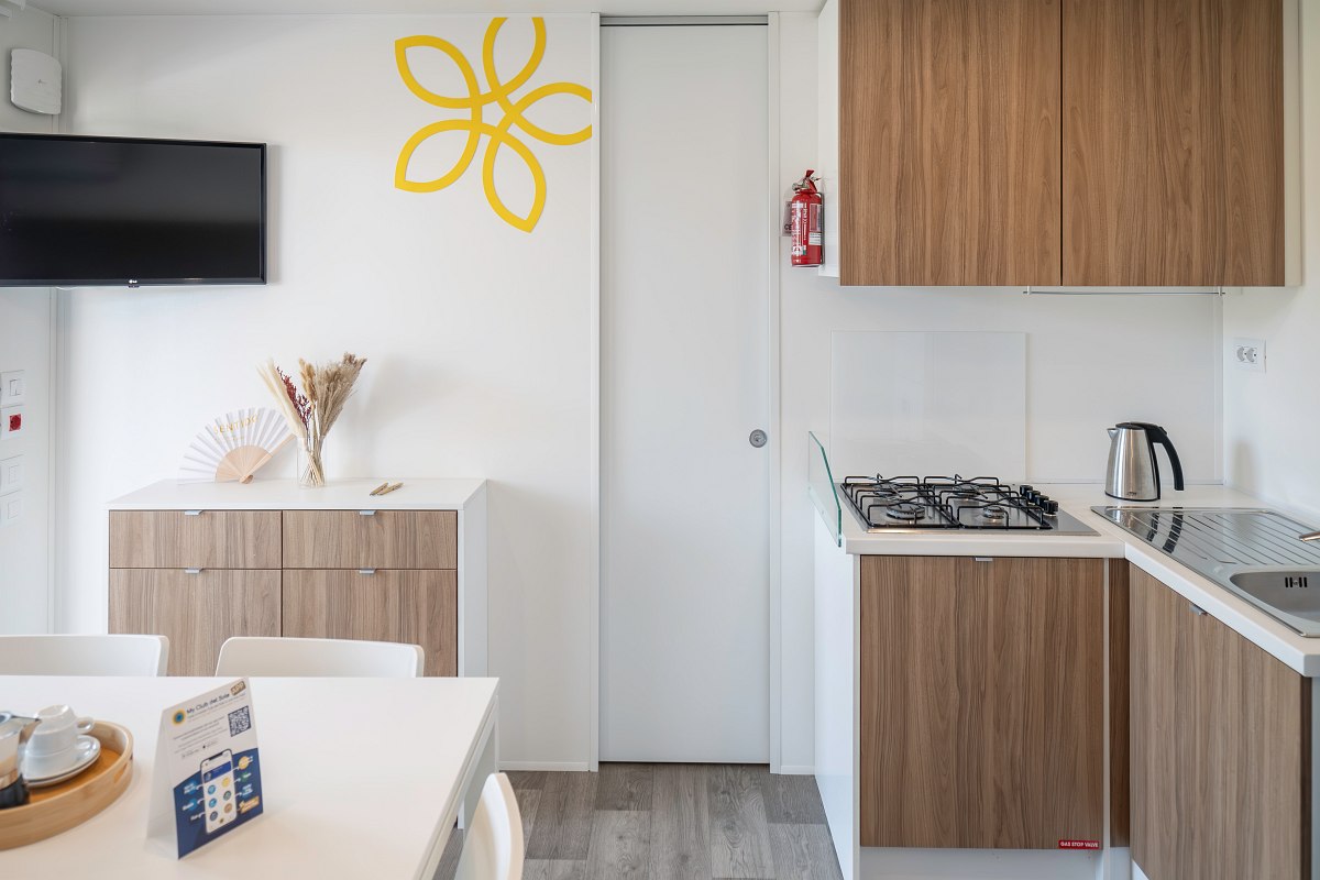 Compact kitchenette with cooker, sink, fridge and dining area - modern, bright and functional furnishings in mobile home.