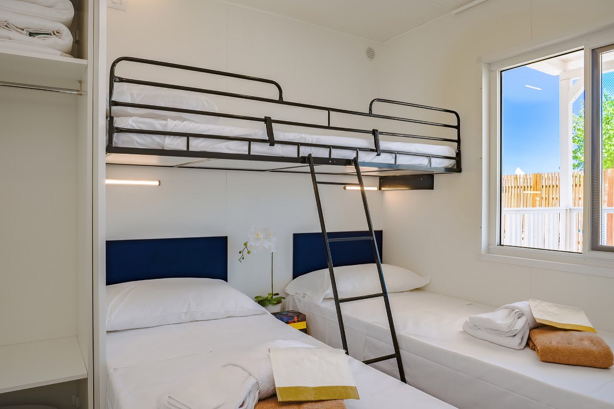 Small bedroom with bunk bed, two single beds, window and storage space - functional and cosy furnishings.