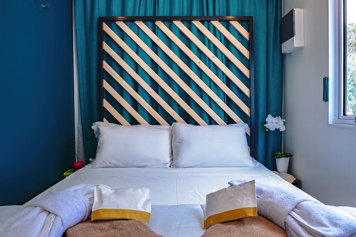 Cosy bedroom with double bed, decorative wooden headboard, blue curtain and fresh towels - stylish and inviting.