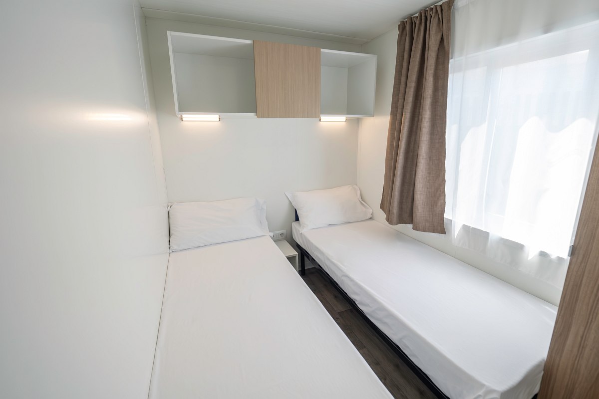 Compact bedroom in the mobile home with two single beds, window, storage space and simple furnishings - modern and functional.