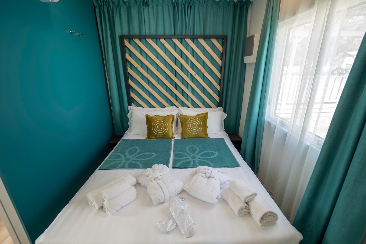 Compact bedroom with double bed, turquoise walls, decorative headboard, curtains and yellow cushions - cosy and modern.