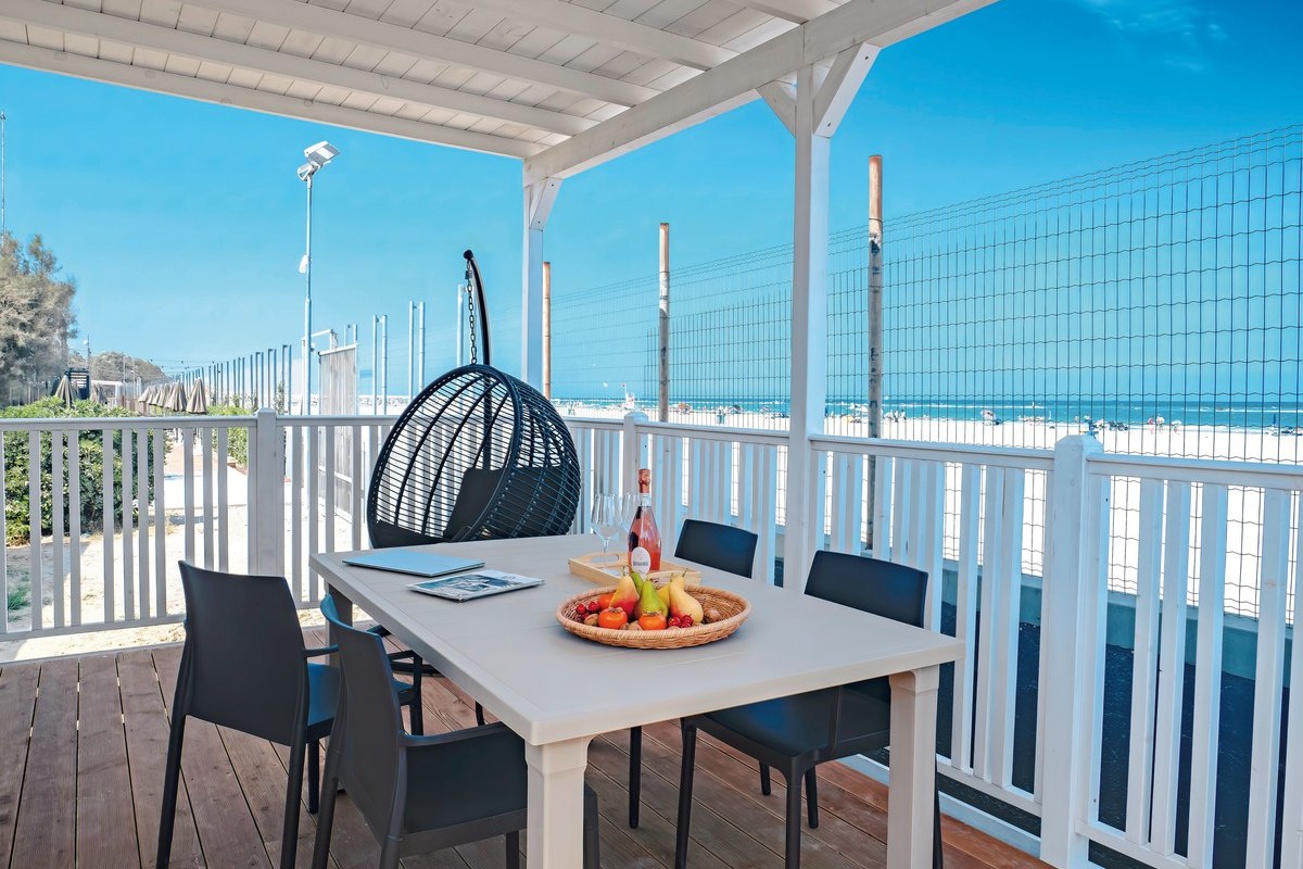 Terrace with white railings, dining table with six chairs, hanging basket and sea view - inviting and sunny.