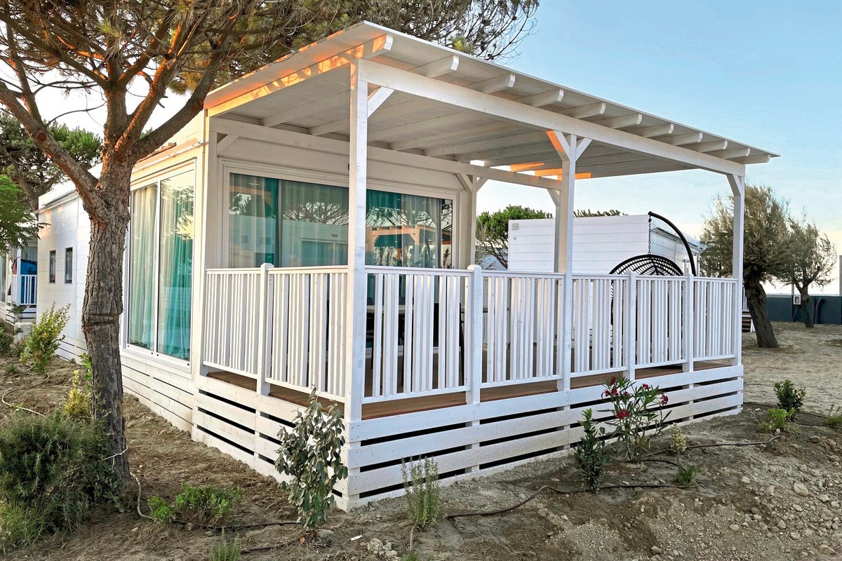 Camp Lodge Elite - Modern mobile home with large, covered wooden terrace, white railings and floor-to-ceiling windows - bright and inviting.