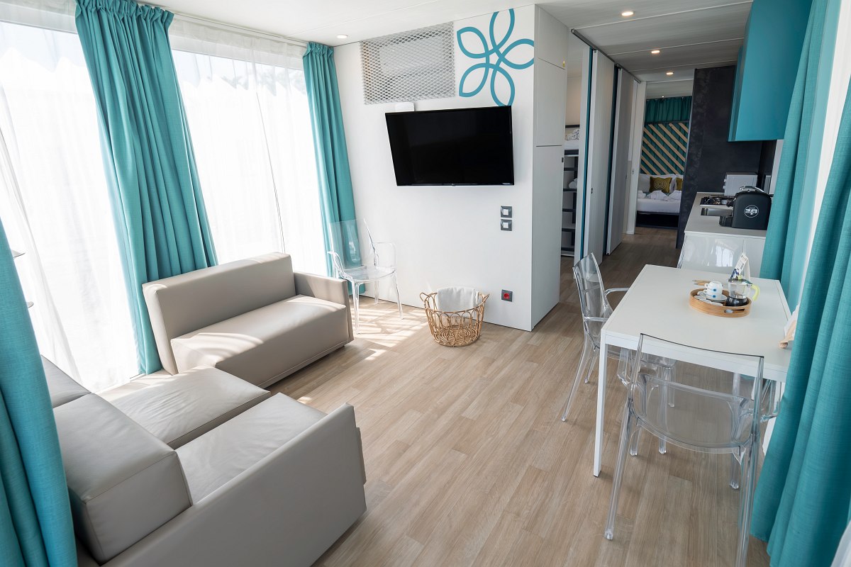 Modern living room with light-coloured furniture, dining table, flat-screen TV and large windows with turquoise-coloured curtains - friendly and airy.