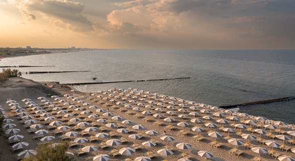 Beach with lots of white parasols and sun loungers, calm sea and evening sky with clouds.