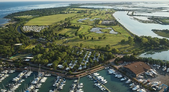 Sentido Tenuta Premium Village, Location - Aerial view of a marina with numerous boats, neighbouring green golf course and sea view in the background.