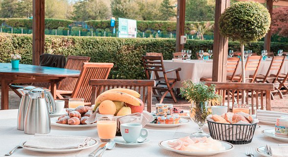 Outdoor breakfast table with coffee, juice, fresh fruit, pastries and cold cuts - set under a wooden terrace in the garden.