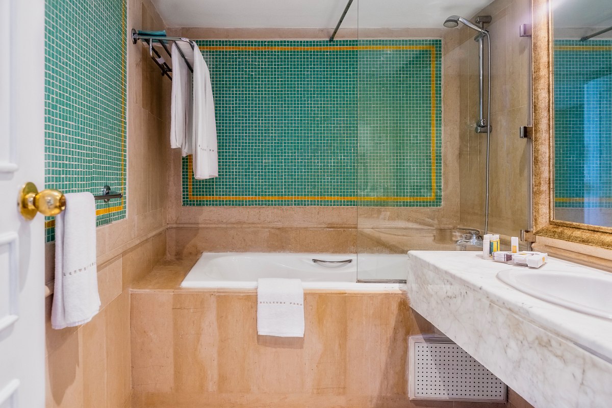 Chambre d'hôtel moderne avec un grand lit double, des sols en bois clair, des couleurs neutres et des lampes murales élégantes.